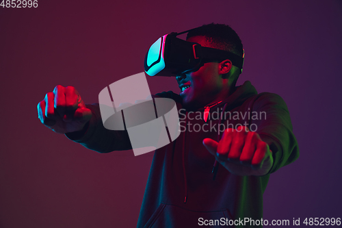 Image of African-american man\'s portrait in VR-headset isolated on gradient studio background in neon light
