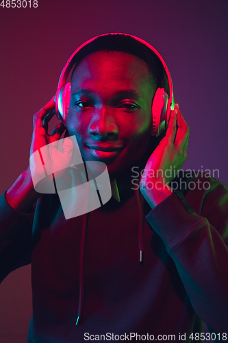 Image of African-american man\'s portrait with headphones isolated on gradient studio background in neon light