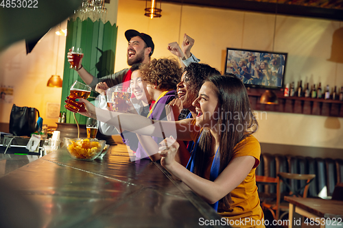 Image of Sport fans cheering at bar, pub and drinking beer while championship, competition is going