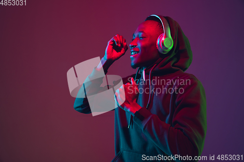 Image of African-american man\'s portrait with headphones isolated on gradient studio background in neon light