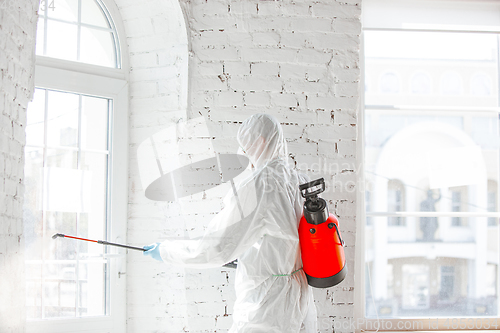 Image of Coronavirus Pandemic. A disinfector in a protective suit and mask sprays disinfectants in the house or office