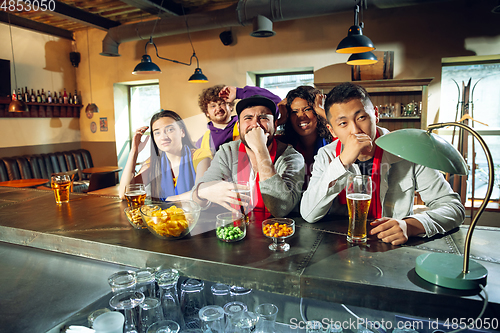 Image of Sport fans cheering at bar, pub and drinking beer while championship, competition is going