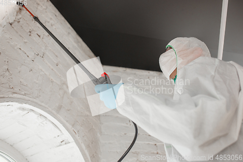Image of Coronavirus Pandemic. A disinfector in a protective suit and mask sprays disinfectants in the house or office