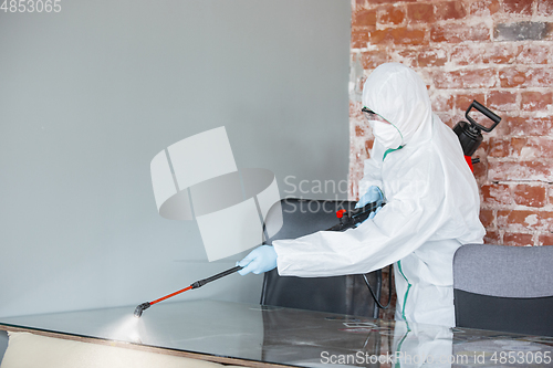 Image of Coronavirus Pandemic. A disinfector in a protective suit and mask sprays disinfectants in the house or office