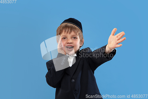 Image of Portrait of a young orthodox jewish boy isolated on blue studio background, meeting the Passover