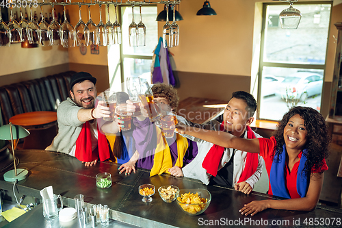 Image of Sport fans cheering at bar, pub and drinking beer while championship, competition is going