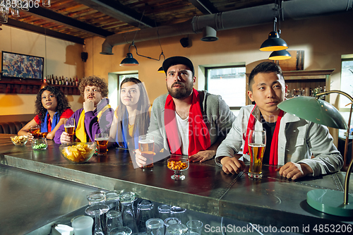 Image of Sport fans cheering at bar, pub and drinking beer while championship, competition is going