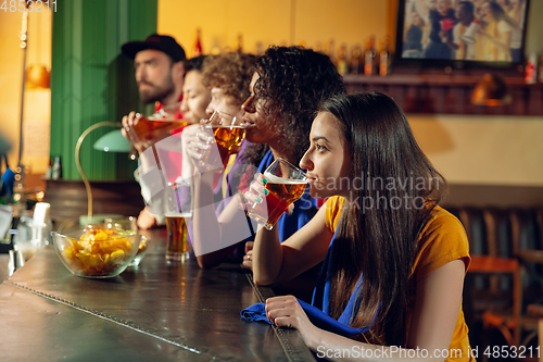 Image of Sport fans cheering at bar, pub and drinking beer while championship, competition is going