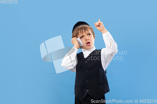 Image of Portrait of a young orthodox jewish boy isolated on blue studio background, meeting the Passover