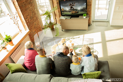 Image of Excited family watching american football, sport match at home
