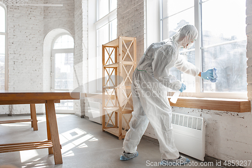 Image of Coronavirus Pandemic. A disinfector in a protective suit and mask sprays disinfectants in the house or office