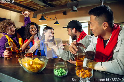 Image of Sport fans cheering at bar, pub and drinking beer while championship, competition is going