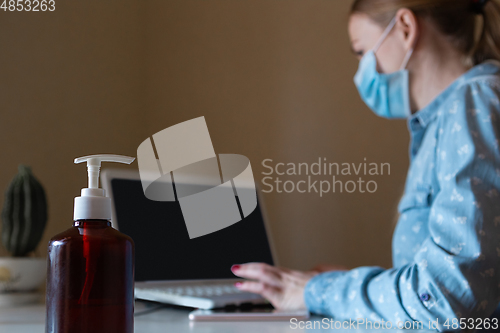 Image of Young woman in face mask disinfecting gadgets surfaces on her workplace