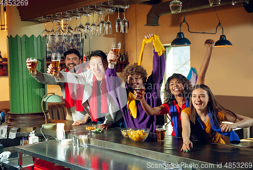 Image of Sport fans cheering at bar, pub and drinking beer while championship, competition is going