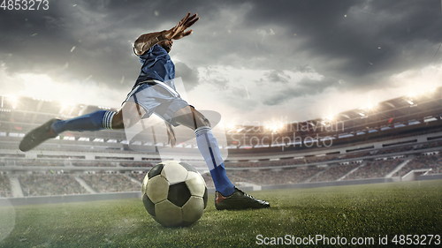 Image of Football or soccer player in action on stadium with flashlights, kicking ball for winning goal, wide angle