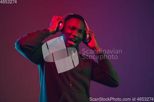 Image of African-american man\'s portrait with headphones isolated on gradient studio background in neon light