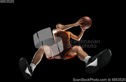 Image of Young professional basketball player in action, motion isolated on black background, look from the bottom. Concept of sport, movement, energy and dynamic.