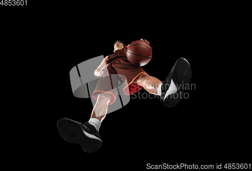 Image of Young professional basketball player in action, motion isolated on black background, look from the bottom. Concept of sport, movement, energy and dynamic.