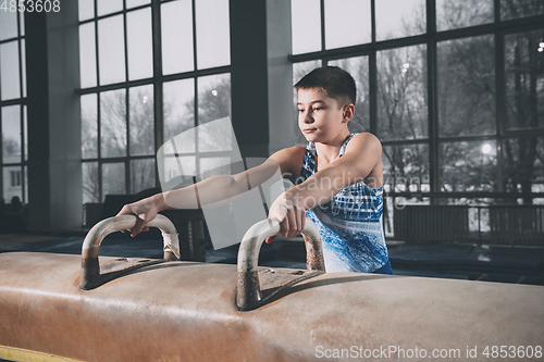 Image of Little male gymnast training in gym, flexible and active. Caucasian fit little boy, athlete in sportswear practicing in exercises for strength, balance.