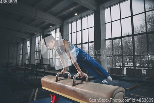 Image of Little male gymnast training in gym, flexible and active. Caucasian fit little boy, athlete in sportswear practicing in exercises for strength, balance.