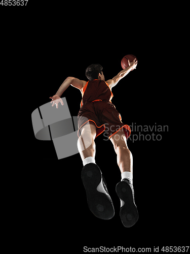 Image of Young professional basketball player in action, motion isolated on black background, look from the bottom. Concept of sport, movement, energy and dynamic.