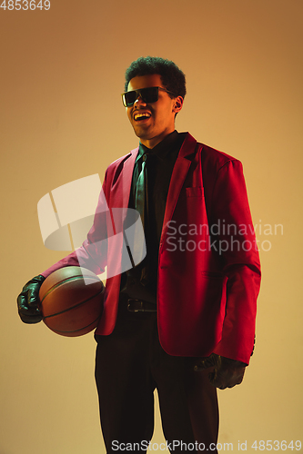 Image of High-fashion styled man in red jacket playing basketball isolted over brown background