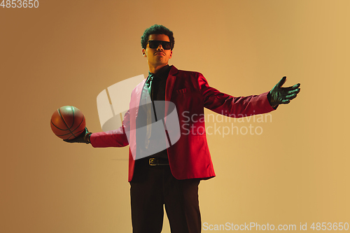 Image of High-fashion styled man in red jacket playing basketball isolted over brown background