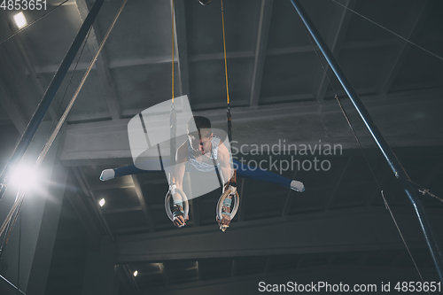 Image of Little male gymnast training in gym, flexible and active. Caucasian fit little boy, athlete in sportswear practicing in exercises for strength, balance.