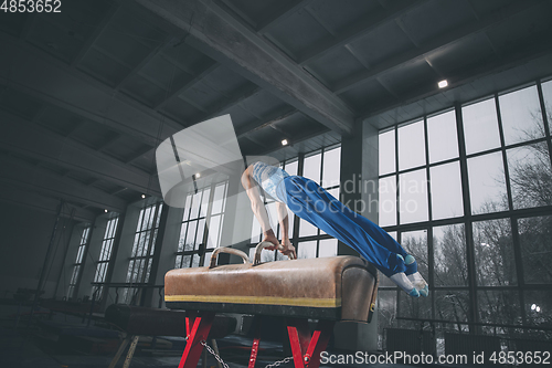 Image of Little male gymnast training in gym, flexible and active. Caucasian fit little boy, athlete in sportswear practicing in exercises for strength, balance.