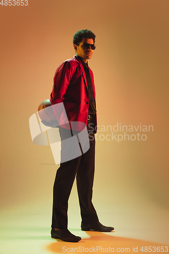 Image of High-fashion styled man in red jacket playing basketball isolted over brown background