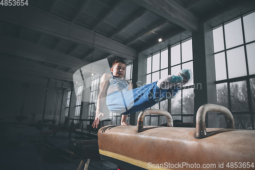 Image of Little male gymnast training in gym, flexible and active. Caucasian fit little boy, athlete in sportswear practicing in exercises for strength, balance.