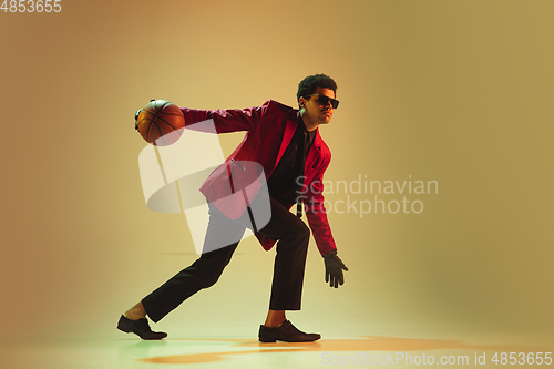 Image of High-fashion styled man in red jacket playing basketball isolted over brown background