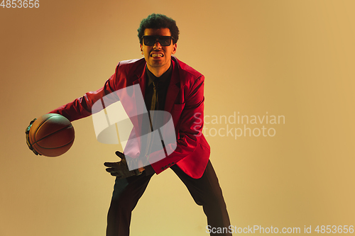 Image of High-fashion styled man in red jacket playing basketball isolted over brown background