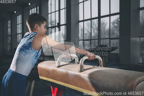 Image of Little male gymnast training in gym, flexible and active. Caucasian fit little boy, athlete in sportswear practicing in exercises for strength, balance.