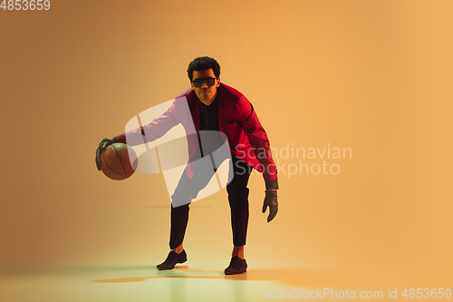 Image of High-fashion styled man in red jacket playing basketball isolted over brown background