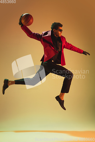 Image of High-fashion styled man in red jacket playing basketball isolted over brown background