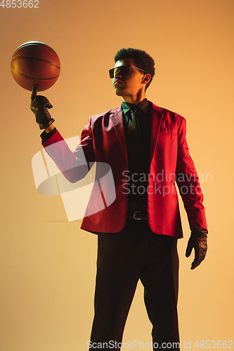 Image of High-fashion styled man in red jacket playing basketball isolted over brown background