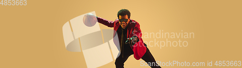 Image of High-fashion styled man in red jacket playing basketball isolted over brown background