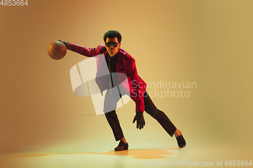 Image of High-fashion styled man in red jacket playing basketball isolted over brown background