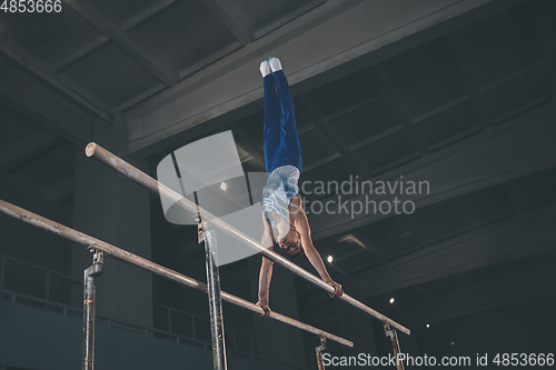 Image of Little male gymnast training in gym, flexible and active. Caucasian fit little boy, athlete in sportswear practicing in exercises for strength, balance.