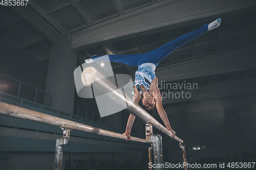 Image of Little male gymnast training in gym, flexible and active. Caucasian fit little boy, athlete in sportswear practicing in exercises for strength, balance.