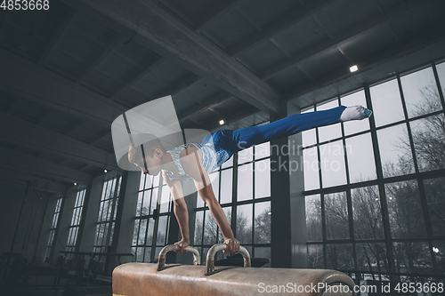 Image of Little male gymnast training in gym, flexible and active. Caucasian fit little boy, athlete in sportswear practicing in exercises for strength, balance.