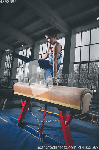 Image of Little male gymnast training in gym, flexible and active. Caucasian fit little boy, athlete in sportswear practicing in exercises for strength, balance.