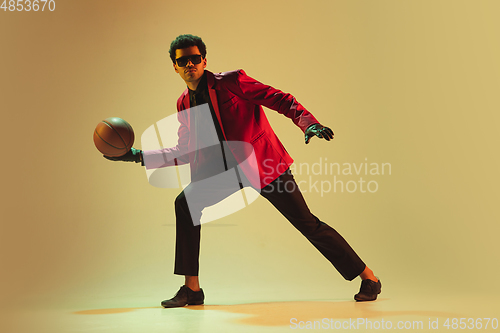 Image of High-fashion styled man in red jacket playing basketball isolted over brown background