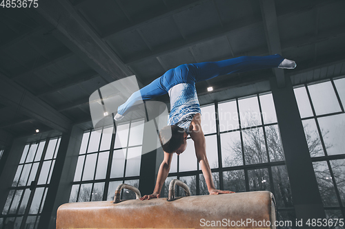 Image of Little male gymnast training in gym, flexible and active. Caucasian fit little boy, athlete in sportswear practicing in exercises for strength, balance.