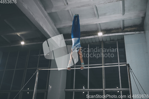 Image of Little male gymnast training in gym, flexible and active. Caucasian fit little boy, athlete in sportswear practicing in exercises for strength, balance.