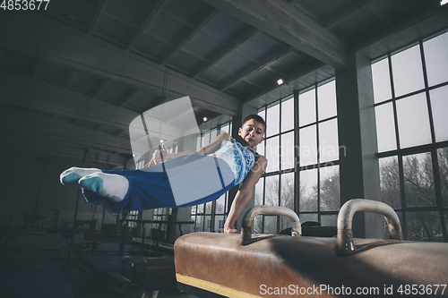 Image of Little male gymnast training in gym, flexible and active. Caucasian fit little boy, athlete in sportswear practicing in exercises for strength, balance.