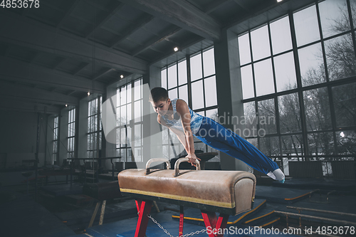 Image of Little male gymnast training in gym, flexible and active. Caucasian fit little boy, athlete in sportswear practicing in exercises for strength, balance.