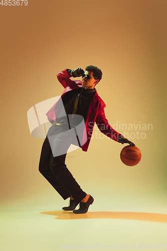 Image of High-fashion styled man in red jacket playing basketball isolted over brown background