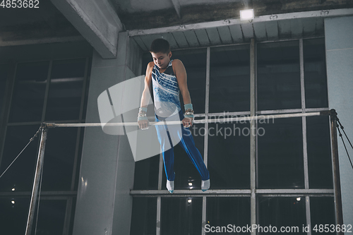 Image of Little male gymnast training in gym, flexible and active. Caucasian fit little boy, athlete in sportswear practicing in exercises for strength, balance.